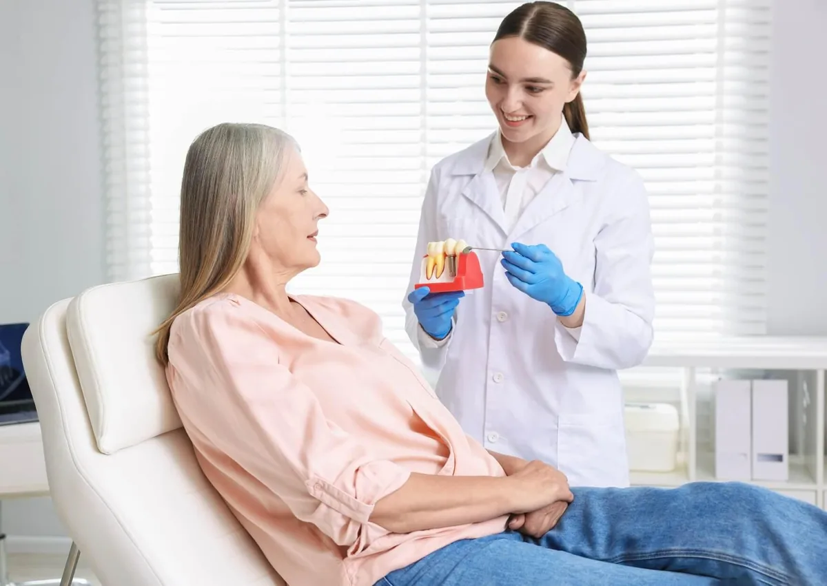 Dentist explaining the tooth implant timeline to a patient using a dental implant model.