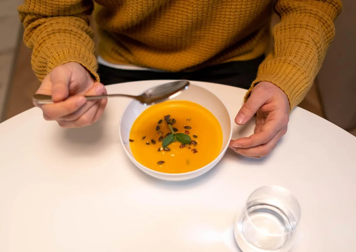 Person eating soft soup as a recommended food option after dental implant surgery.